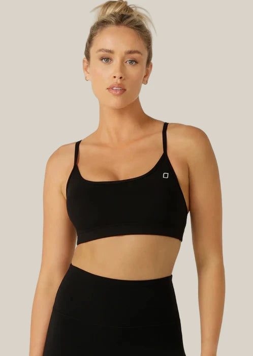 Woman wearing a black sports bra and leggings on a light gray background
