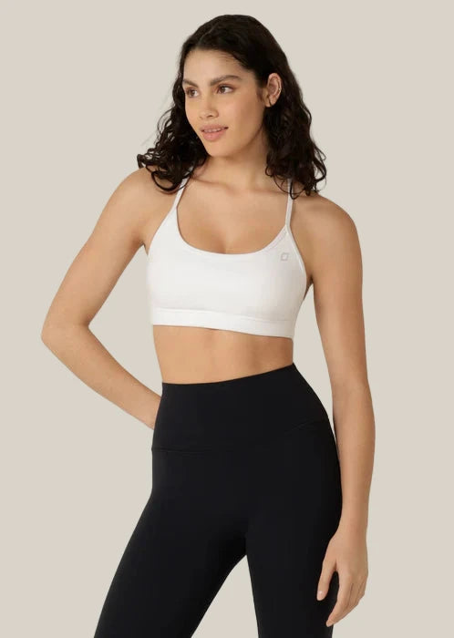 Woman wearing a white sports bra and black leggings on a light gray background