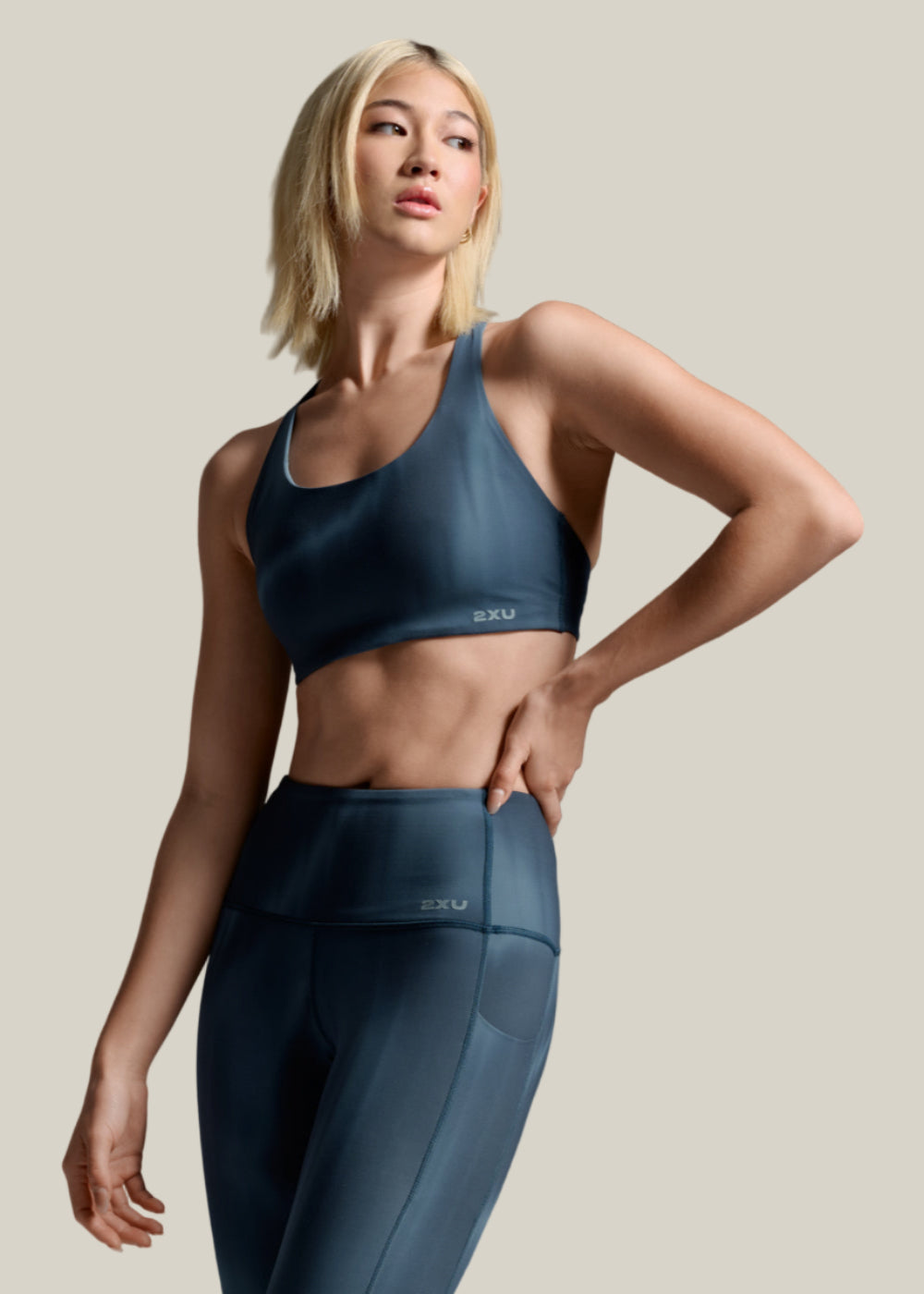 Woman wearing a blue sports bra and leggings on a gray background