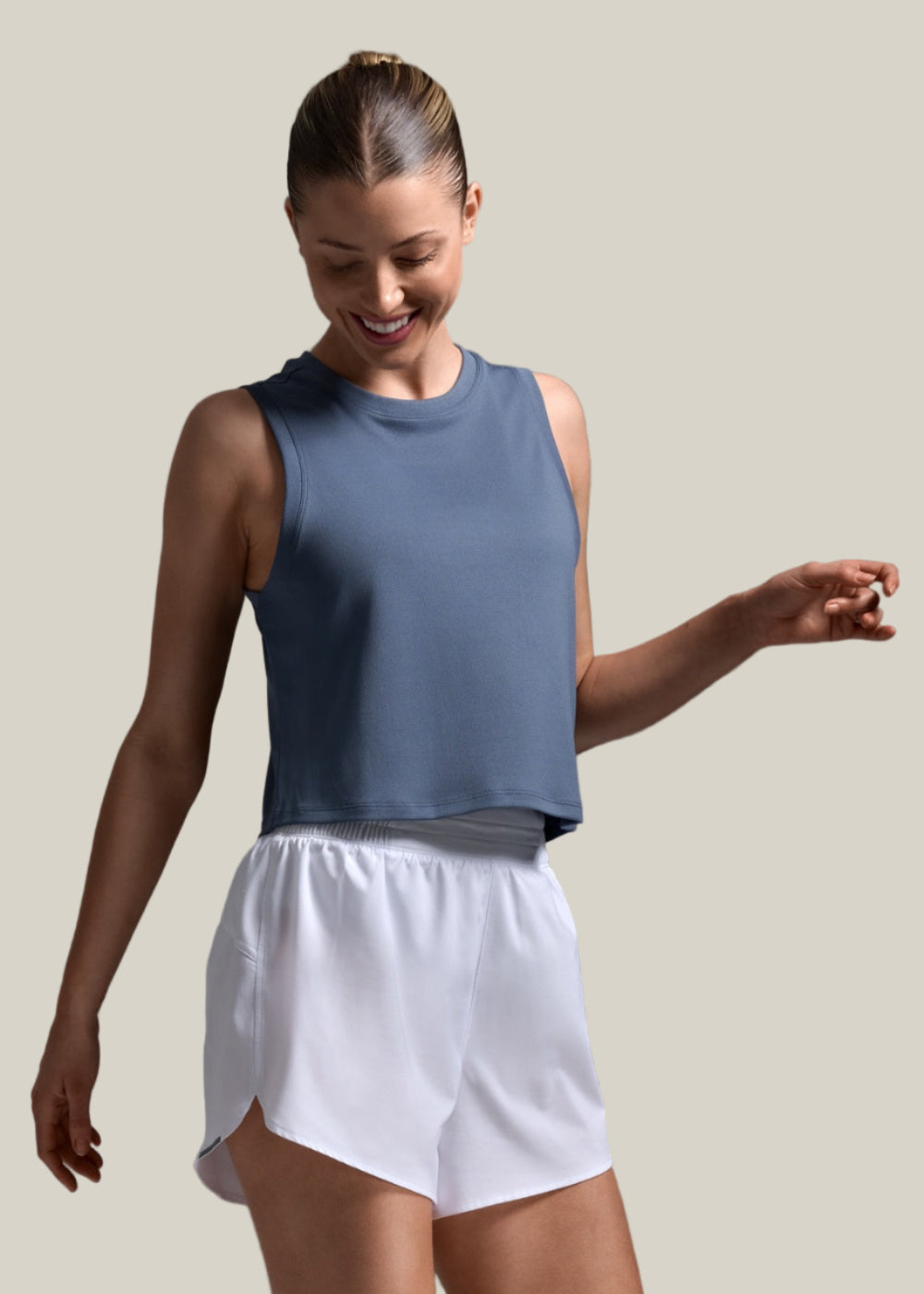 Woman wearing a blue sleeveless top and white shorts on a gray background