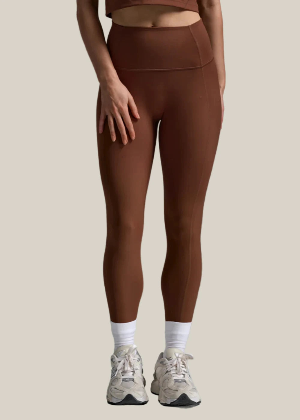 Person wearing brown leggings and white sneakers on a gray background