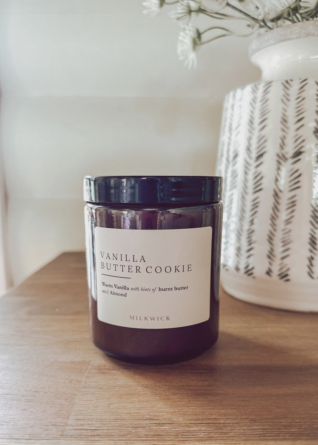 Vanilla butter cookie candle on a wooden surface with a decorative vase in the background