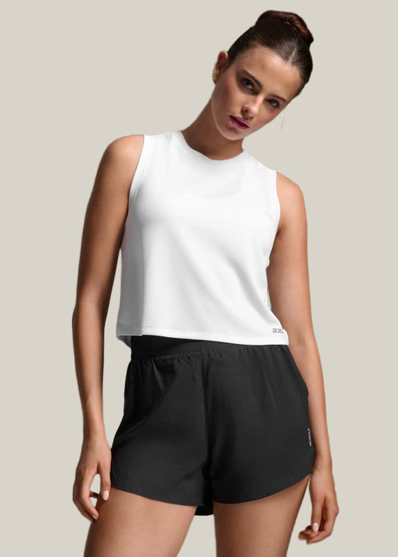 Woman wearing a white sleeveless top and black shorts against a gray background